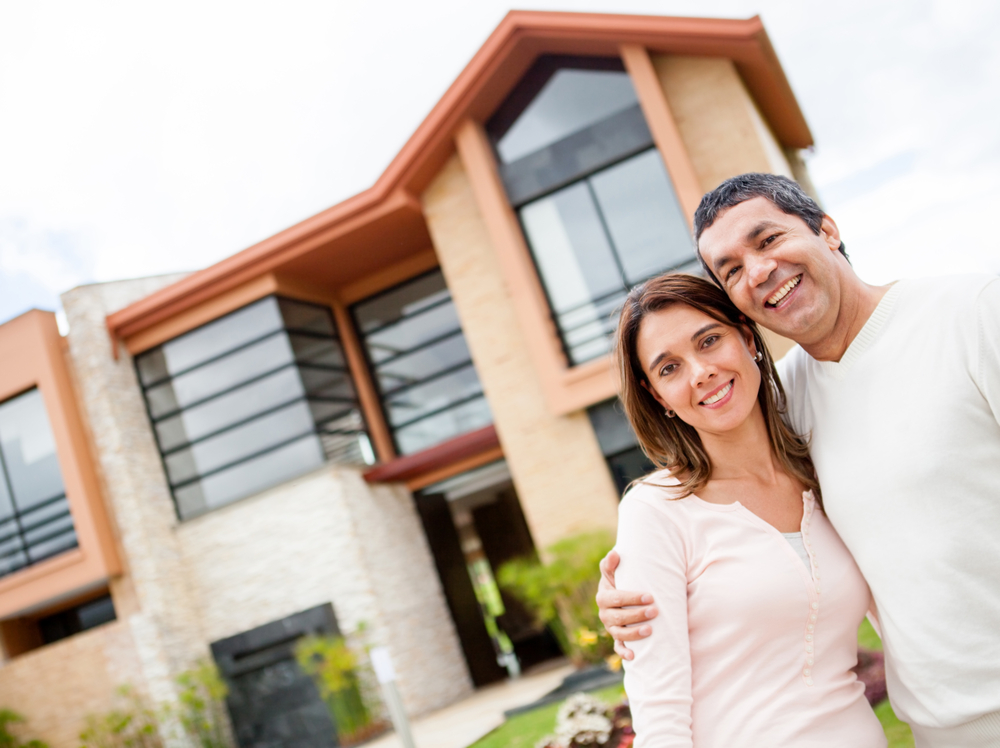 Happy couple with their new house at the background and smiling Happy couple with their new house at the background and smiling